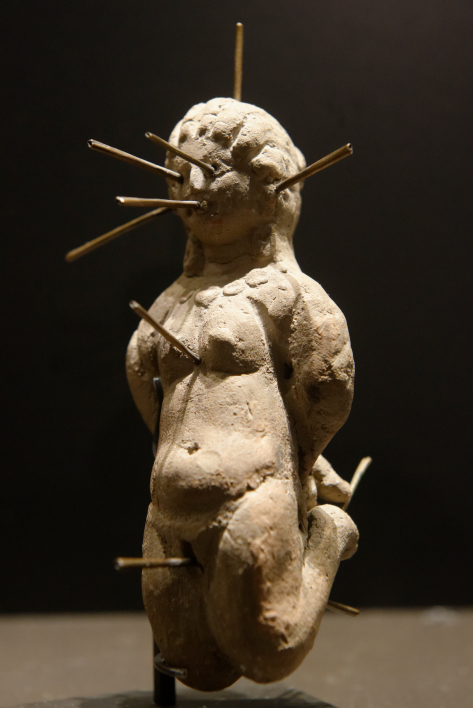 Dagyde représentant une femme nue agenouillée et attachée, percée de treize épingles. Découvert dans un vase en terre cuite contenant également une tablette en plomb portant une défixion. Argile et bronze, IVe siècle ap. J.-C. , musée du Louvre